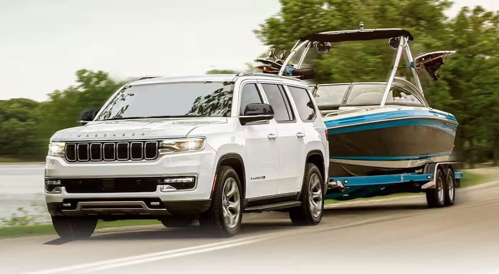 A white 2024 Jeep Wagoneer is shown towing a boat.