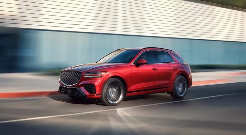 A red 2025 Genesis GV70 is shown driving on a racetrack.