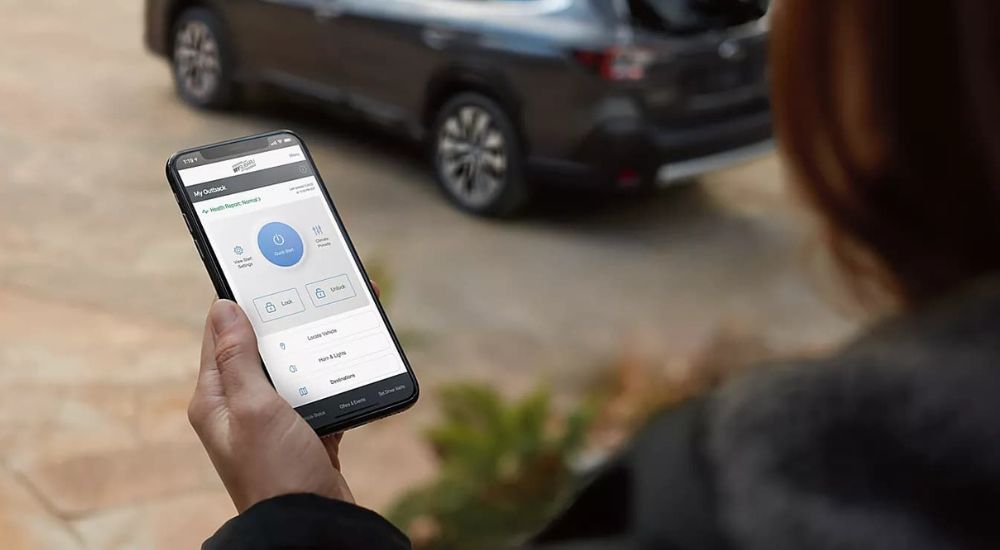 A person is shown looking at the MySubaru app near a 2024 Subaru Outback. 