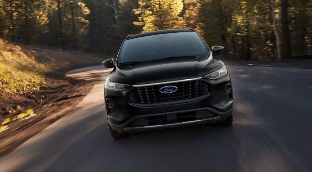 A black 2024 Ford Escape is shown driving on a back road.