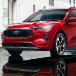 A red 2024 Ford Escape is shown parked on a parking spot near a Ford dealer.