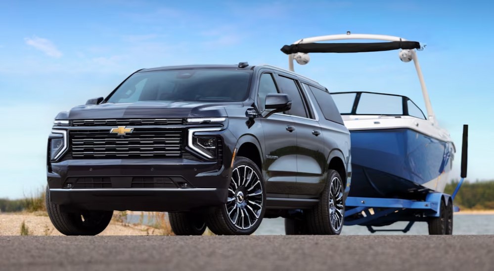 A blue 2025 Chevy Suburban High Country is shown towing a boat.