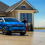A family walking to a blue 2024 Chevy Equinox EV parked in their driveway.