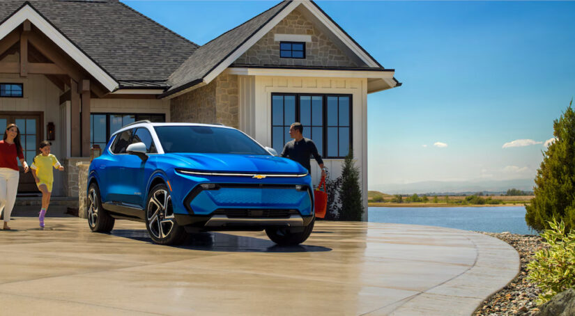 A family walking to a blue 2024 Chevy Equinox EV parked in their driveway.