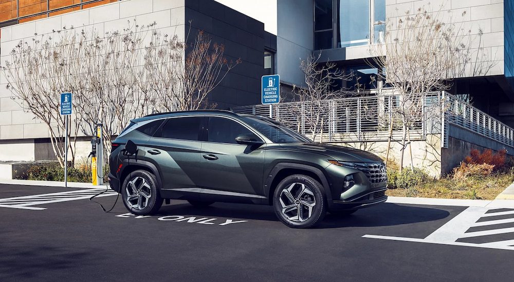 A green 2024 Hyundai Tucson PHEV plugged in at a public EV charging station.