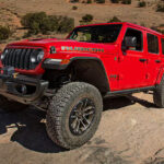 A red 2024 Jeep Wrangler Rubicon driving uphill on a rocky trail.