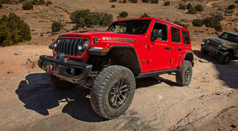 A red 2024 Jeep Wrangler Rubicon driving uphill on a rocky trail.