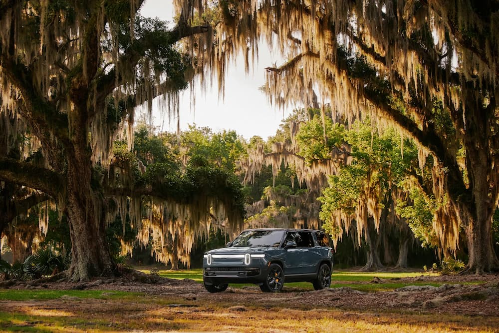 A blue 2024 Rivian R1S is shown parked off-road.