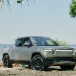 A gray 2024 Rivian R1T is shown parked near an ocean.