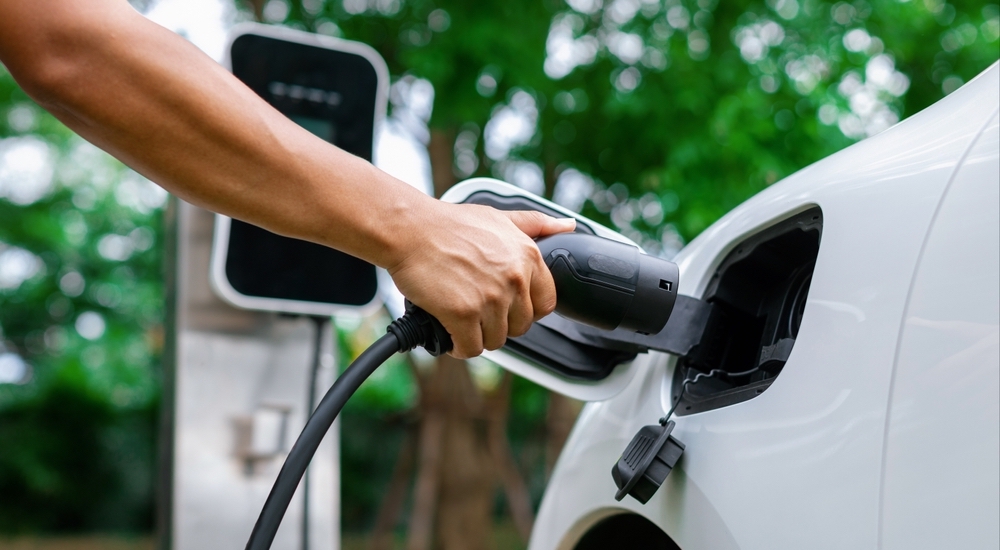 A hand plugging a charger into a white electric vehicle.