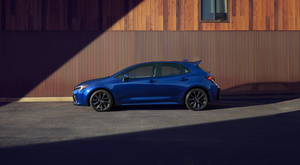 A side angle view of a blue 2025 Toyota Corolla Hatchback parked by a building.