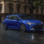 A blue 2025 Toyota Corolla Hatchback driving in a rainy city.