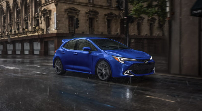 A blue 2025 Toyota Corolla Hatchback driving in a rainy city.