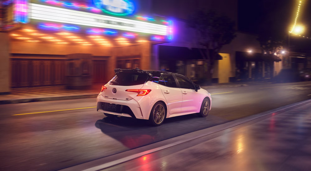 A white 2025 Toyota Corolla Hatchback driving by a theatre.