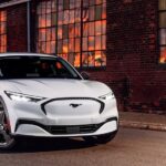 A white 2024 Ford Mustang Mach-E for sale parked by a brick wall.