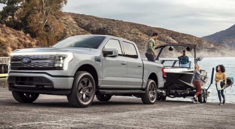 A silver 2024 Ford F-150 Lightning for sale is shown towing a boat.