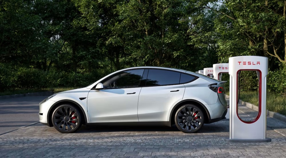 A white 2024 Tesla Model Y is shown parked near a Tesla charge station.