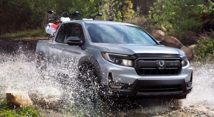 A silver 2025 Honda Ridgeline Sport is shown driving off-road after visiting a Honda dealer.