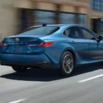 A blue 2025 Toyota Camry for sale is shown from the rear at an angle.