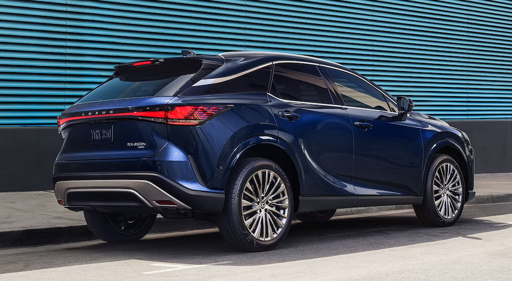 Rear view of a blue 2024 Lexus RX 450 Hybrid parked next to a blue wall.