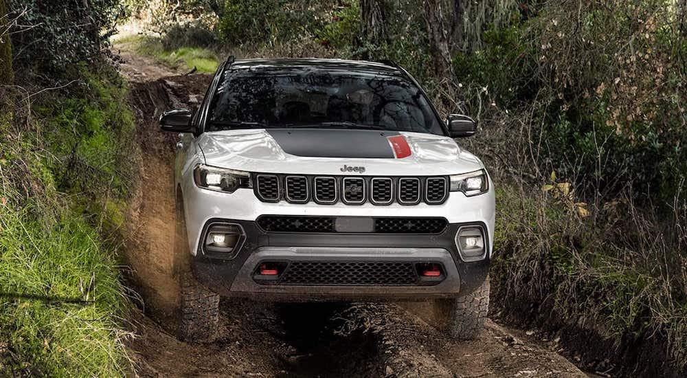 A white 2024 Jeep Compass Trailhawk is shown from the front while off-road.