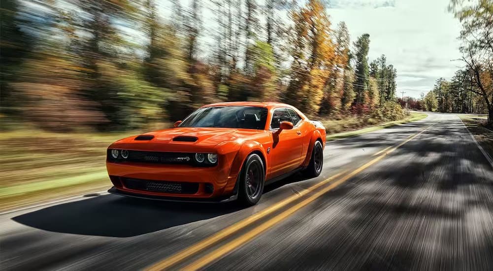 An orange 2023 Dodge Challenger SRT is shown driving on a highway.