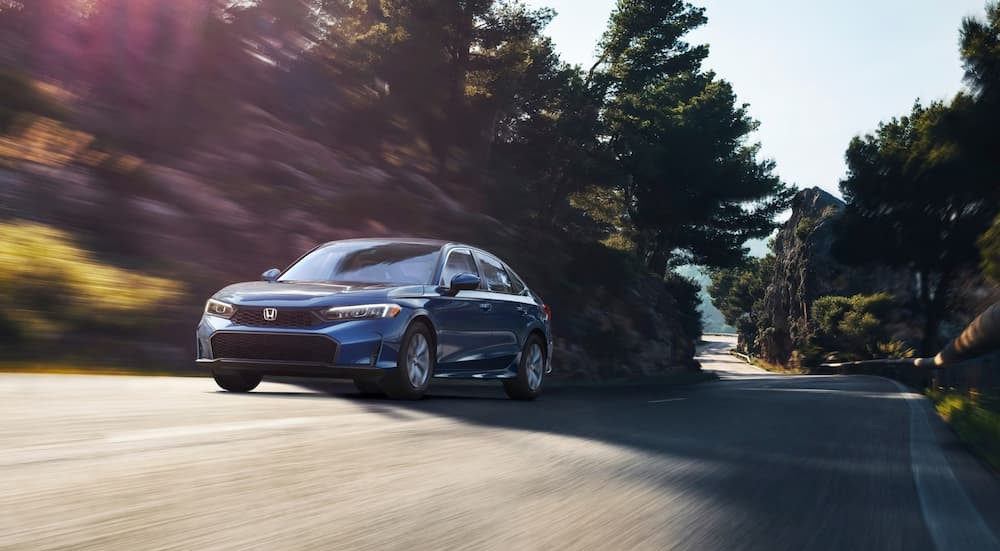 A blue 2025 Honda Civic Hybrid is shown driving on a backroad after visiting a Honda dealer..