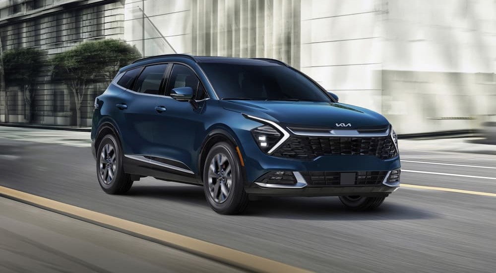 A blue 2025 Kia Sportage Hybrid is shown driving on a city street.