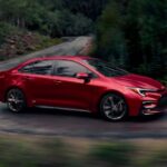 A red 2025 Toyota Corolla Hybrid is shown driving on a backroad.
