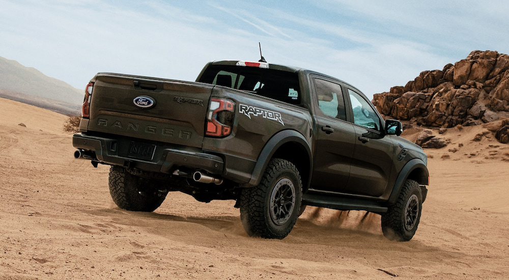 Rear view of a dark green 2024 Ford Ranger Raptor off-roading through sand.