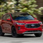 A red 2025 Ford Escape ST-Line Elite driving to a Ford dealer.