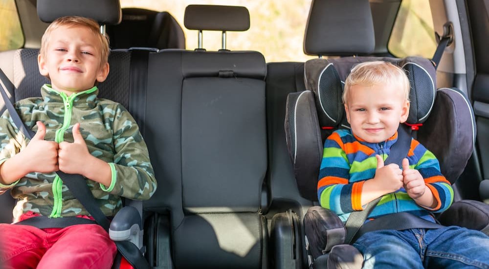 Two children are shown sitting in a booster seat and a child's car seat.