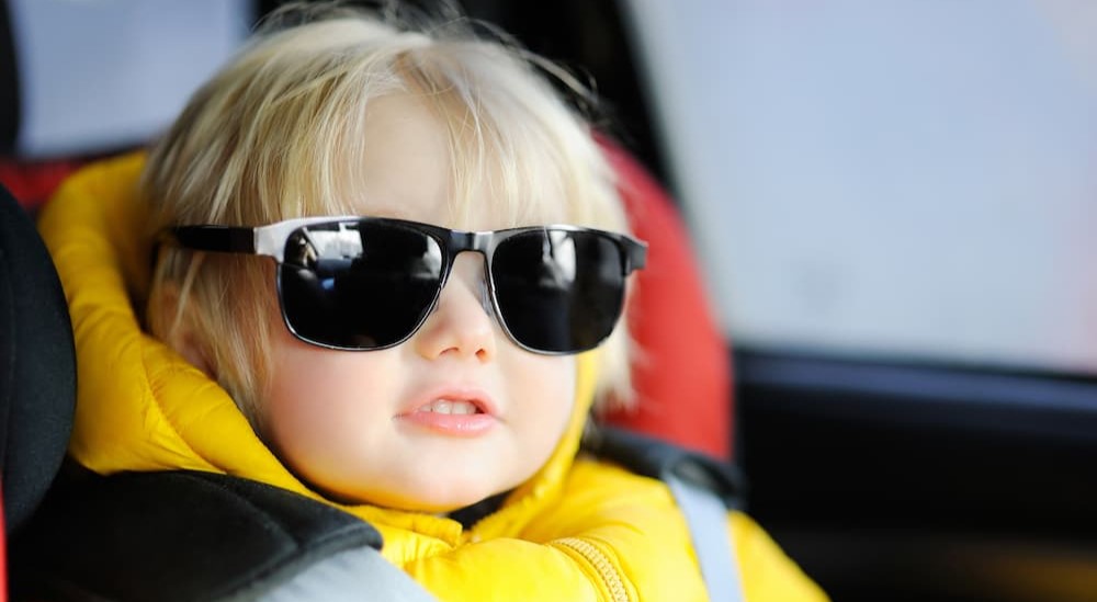 A child wearing sunglasses is shown sitting in a car seat.