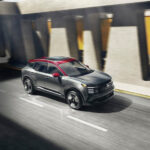 A grey and red 2025 Nissan Kicks SR is shown driving to a Nissan dealer.