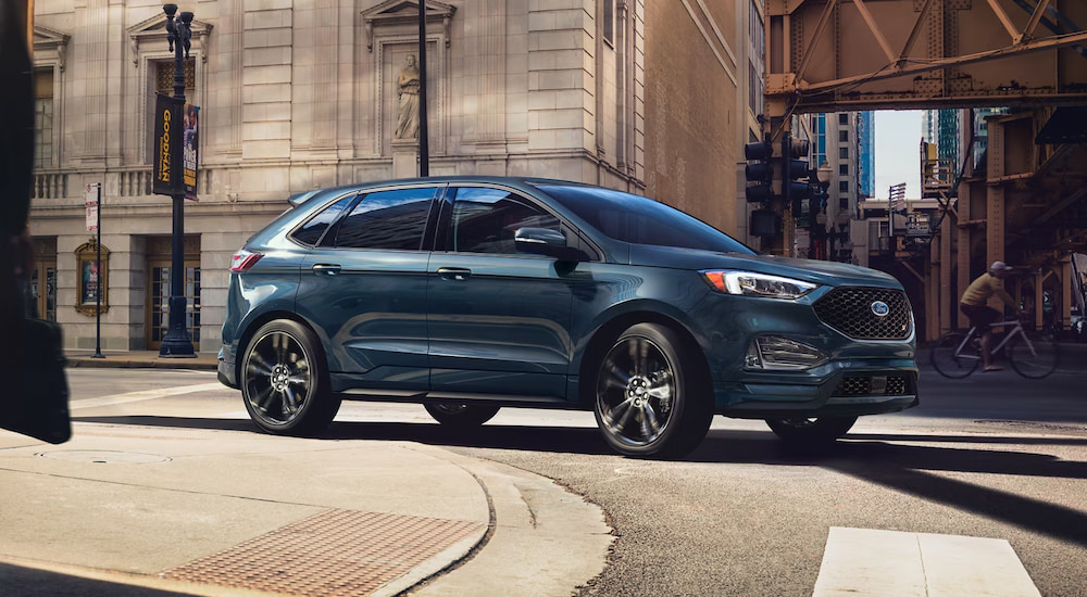 A blue 2024 Ford Edge ST driving around a corner in the city.