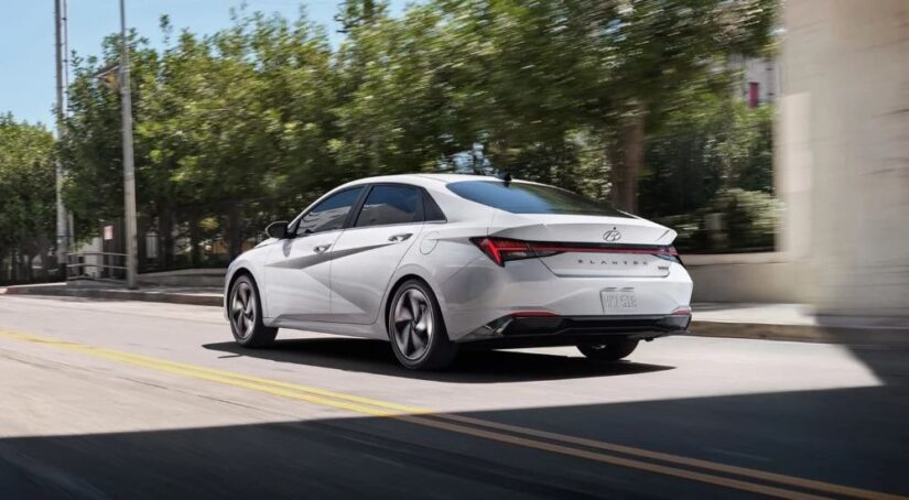 A white 2022 Hyundai Elantra is shown driving on a city street after viewing used cars for sale.