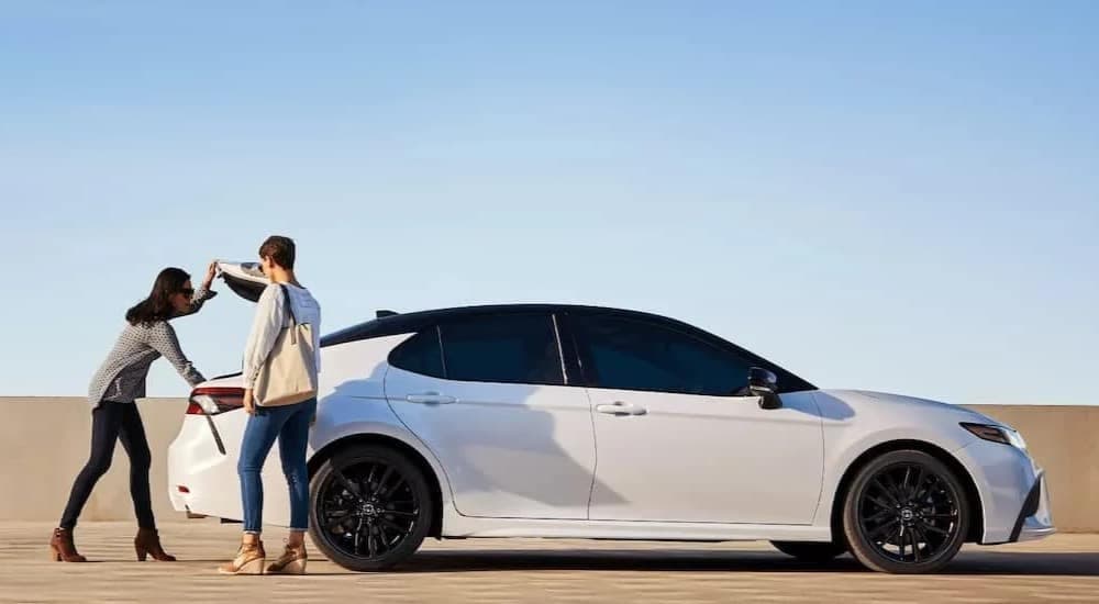 Side view of two women accessing the trunk of a white 2024 Toyota Camry.