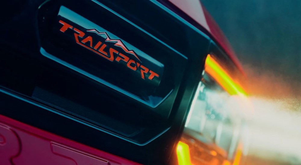 A close-up of the TrailSport badge is shown on the grille of an orange 2026 Honda Passport TrailSport Elite.