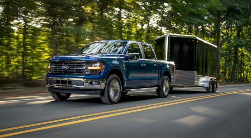 A blue 2024 Ford F-150 for sale in Milan is shown from the front while towing a trailer.