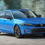 A blue 2025 Honda Civic Hatchback driving through a city.