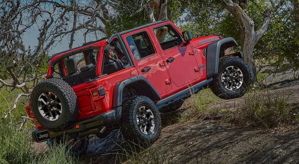 Rear angle view of a red 2025 Jeep Wrangler Rubicon driving up a hill.