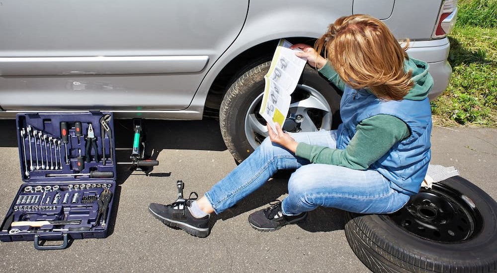 A person holding an owner's manual is shown sitting on a tire near a tool box.