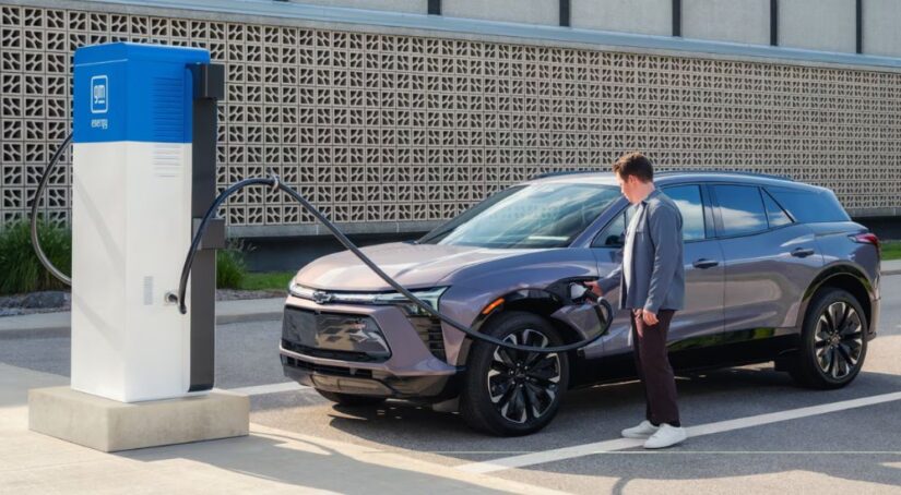 A man plugging in a silver 2025 Chevy Blazer EV RS at a public charging station.