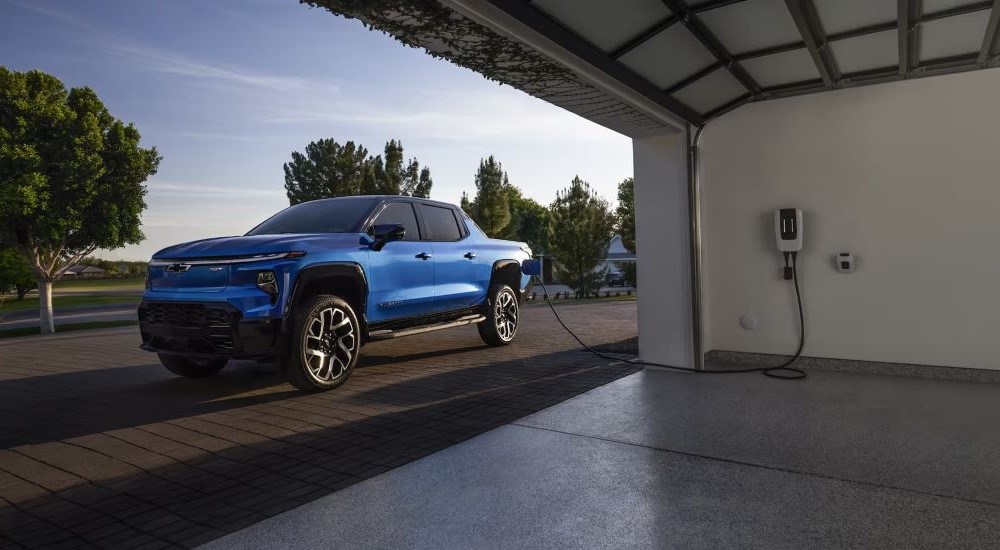 A blue 2025 Chevy Silverado EV RST parked outside a garage and charging.