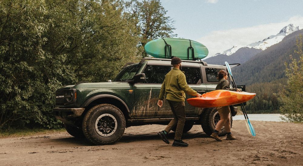 A couple unloading kayaks from the roof of a green 2025 Ford Bronco Badlands.