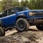 A blue 2025 Ford Bronco Raptor driving off-road over boulders after viewing a Ford Bronco for sale.
