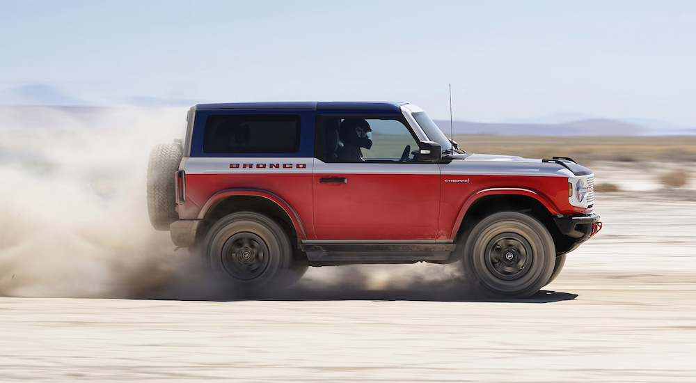 Side view of a red and white 2025 Ford Bronco Stroppe Edition kicking up sand while driving off-road.