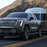 A grey 2025 GMC Sierra EV Denali towing a camper from a GMC dealer.
