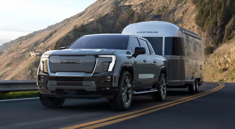 A grey 2025 GMC Sierra EV Denali towing a camper from a GMC dealer.