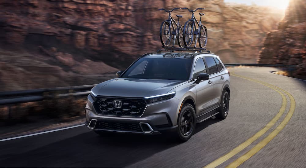 A grey 2025 Honda CR-V Sport Touring Hybrid driving around a bend.